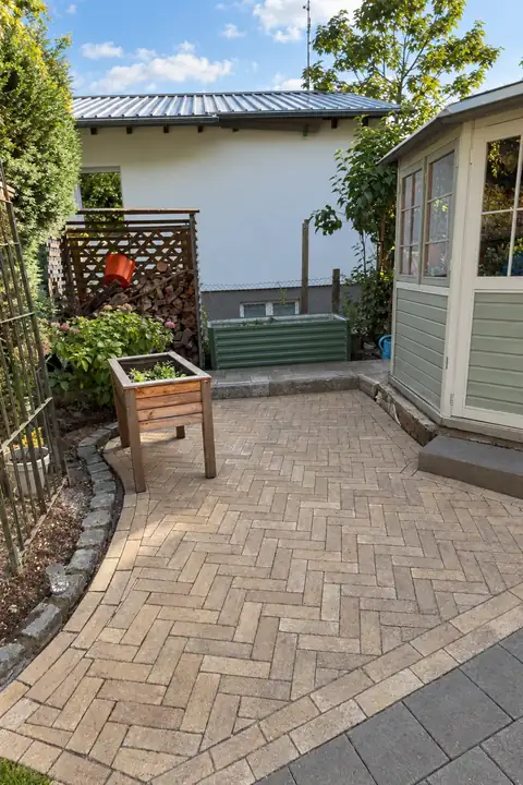 Gartenhof mit Pflaster im Fischgrätverband und dunkler Plattenfläche vor einem Gartenhaus