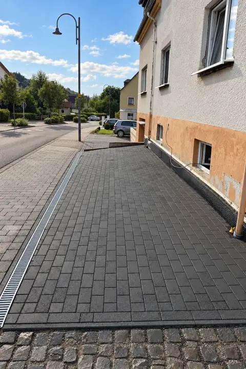 Gepflasterte Hoffläche aus dunkelgrauem Rechteckpflaster mit Entwässerungsrinne am Wohnhaus