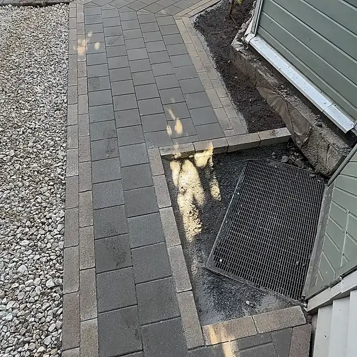 Gepflasterter Weg mit heller Randeinfassung zwischen Kiesfläche und Gartenhaus