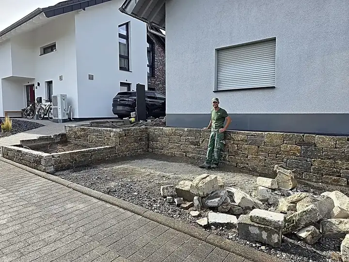 Neue Natursteinmauer in L-Form am Wohnhaus, davor die vorbereitete Fläche