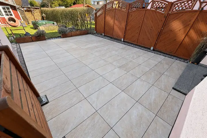 Terrasse aus großformatigen hellen Platten zwischen Holzsichtschutz und Hauswand